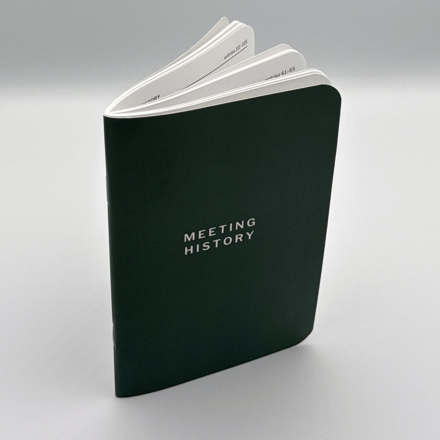Meeting History booklet standing open, pages fanned, dark green cover facing forward.